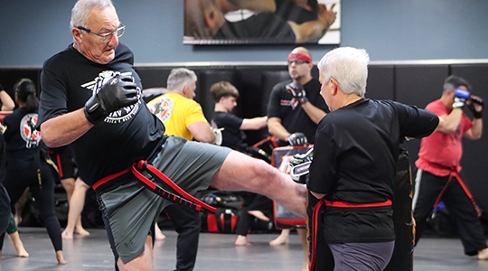 An older man and an older woman do padwork in a Krav Maga class at America's Best Defense.