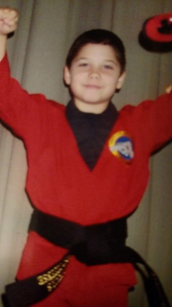 Young martial artist wearing red gi top and black belt flexing his muscles.