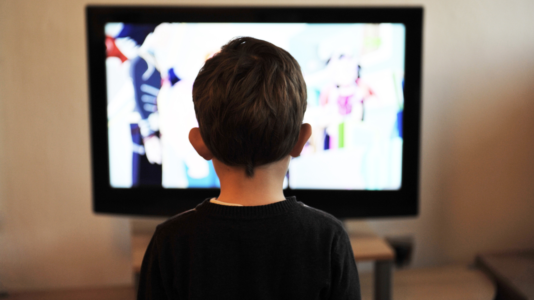 Image of a young boy with short brown hair watching TV with his back to the camera.